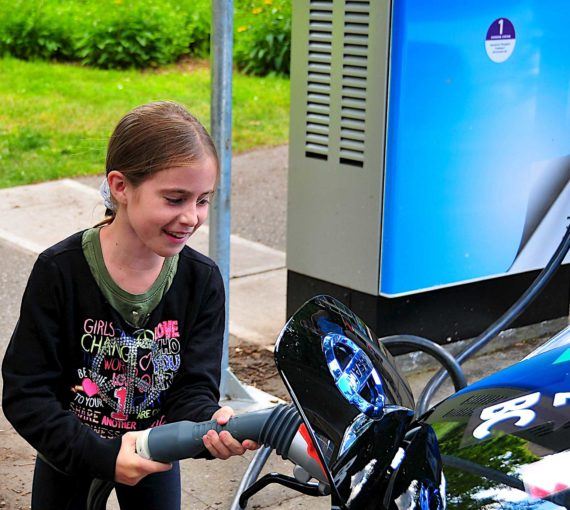 girl-charging-electric-vehicle A young girl plugs in an electric vehicle to charge