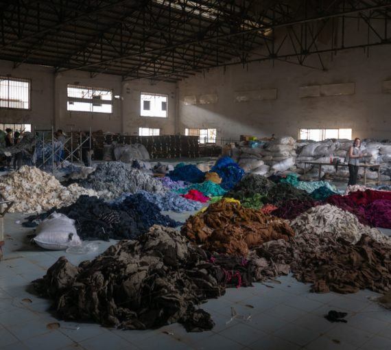 clothing-fabric-piles-factory-sorting-sustainability Clothing fabrics sorted into piles